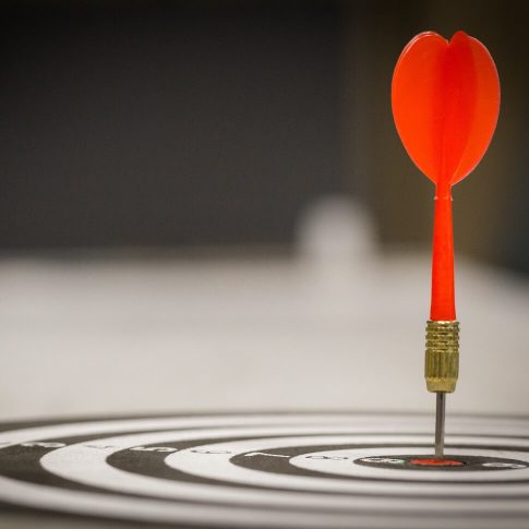 Red dart arrow hitting in the target center of dartboard on bullseye with sun light vintage style, Target marketing and business success concept - Ima@2x-opt